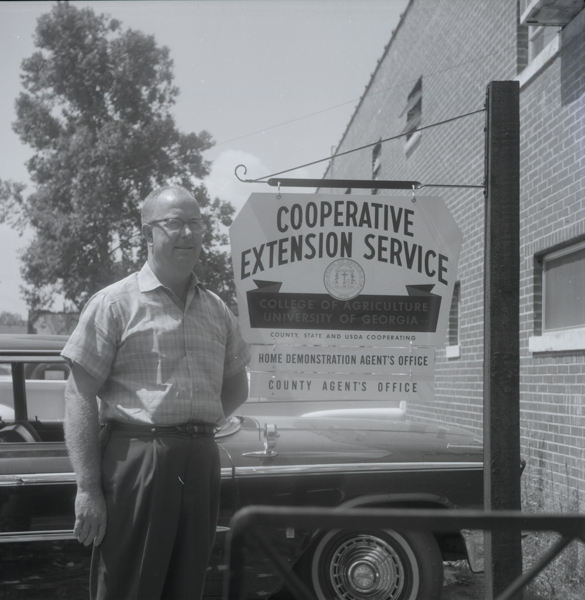 A man stands beside a sign for the Cooperative Extension Service county agent's office